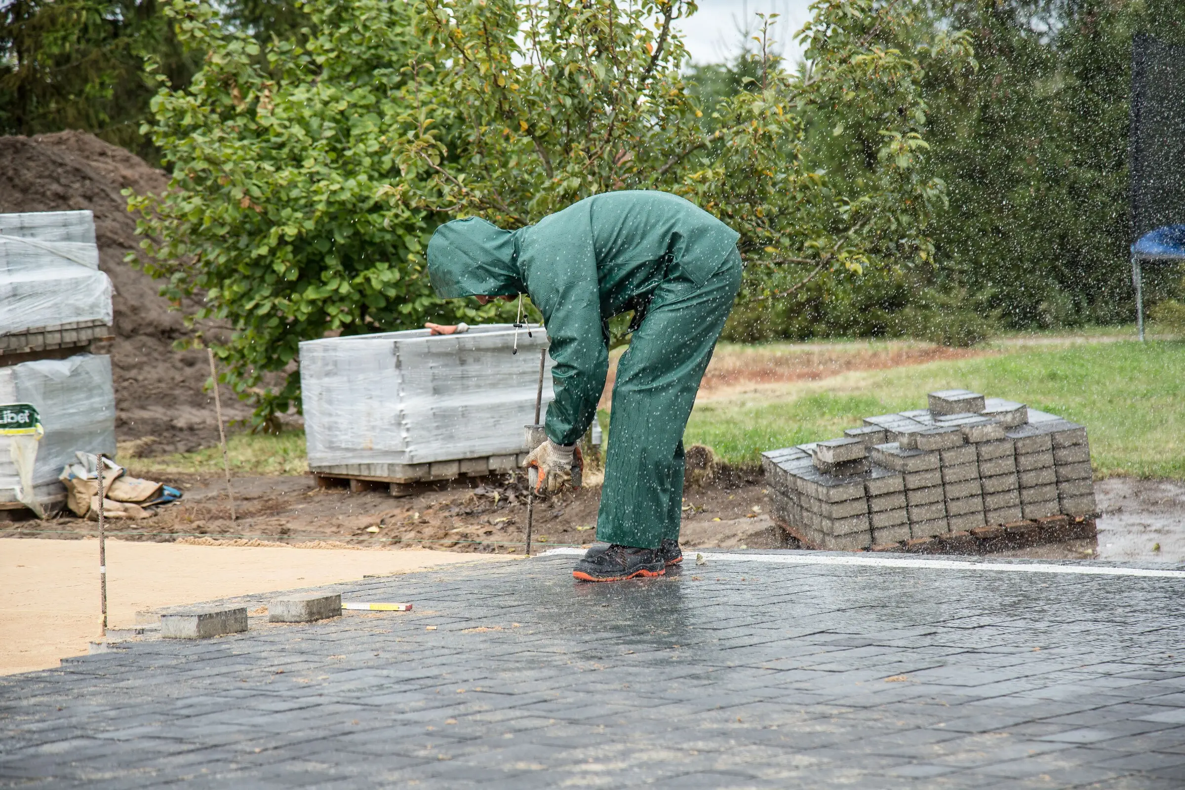 Block paving being laid on a screeded sand bed in the rain, with banded packs of blocks alongside