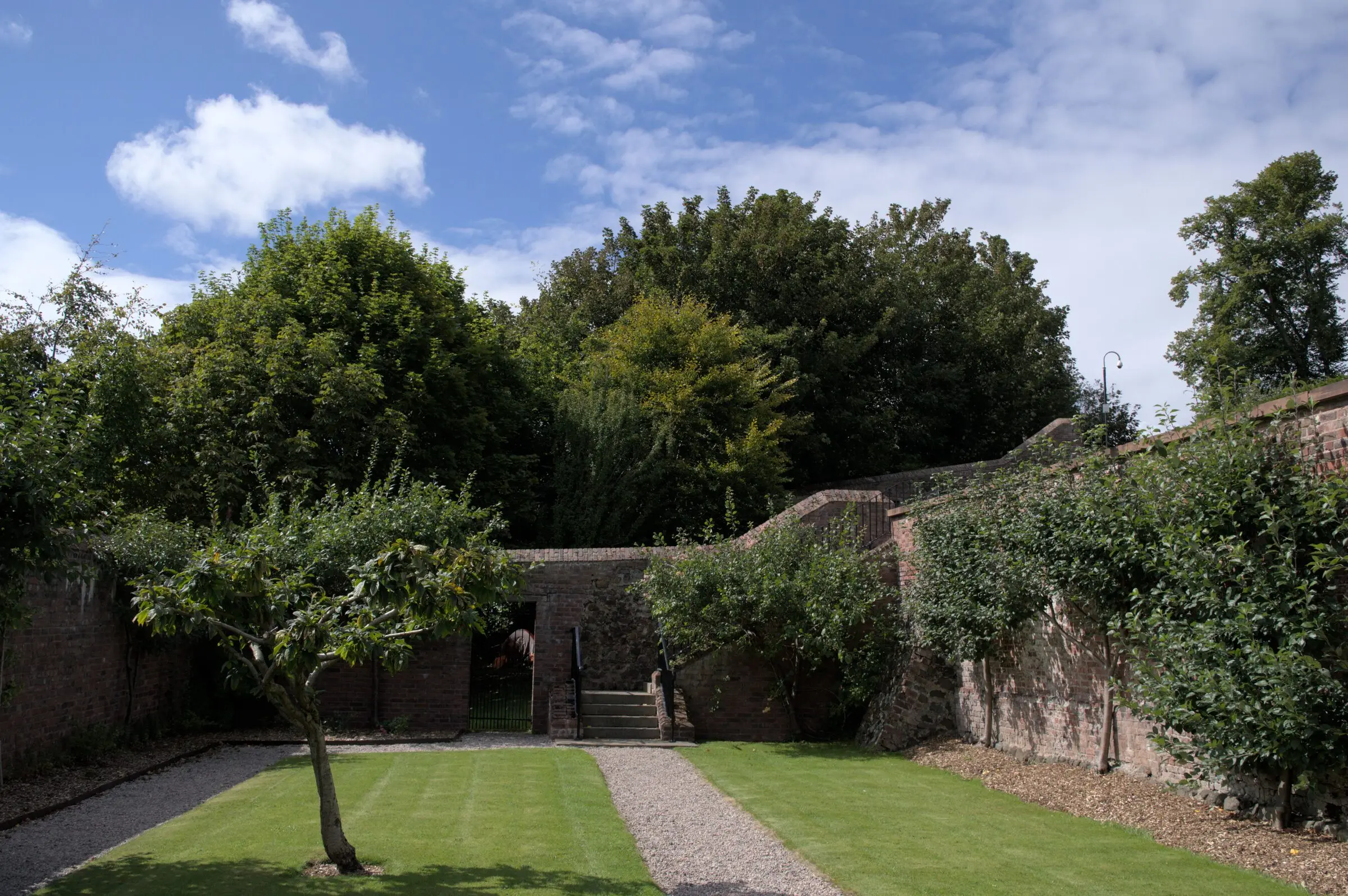 Old red brick walled garden with trained fruit trees, gravel paths and a striped mown lawn